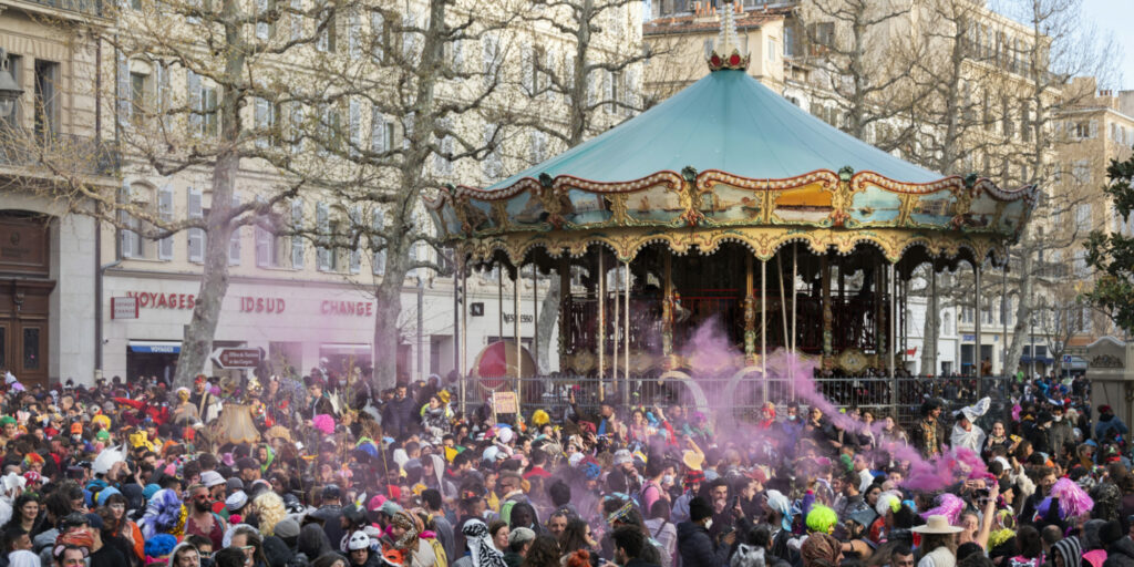 Une foule de Marseillais fêtent le carnaval devant un manège
